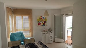 Een eetruimte met een tafel gedekt voor twee personen, een stoel, een kast met lades, een hangend horloge en een deur die naar buiten leidt.