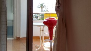 Een kamer met een bed, een schuifdeur naar een balkon met een rode stoel en een tafel.