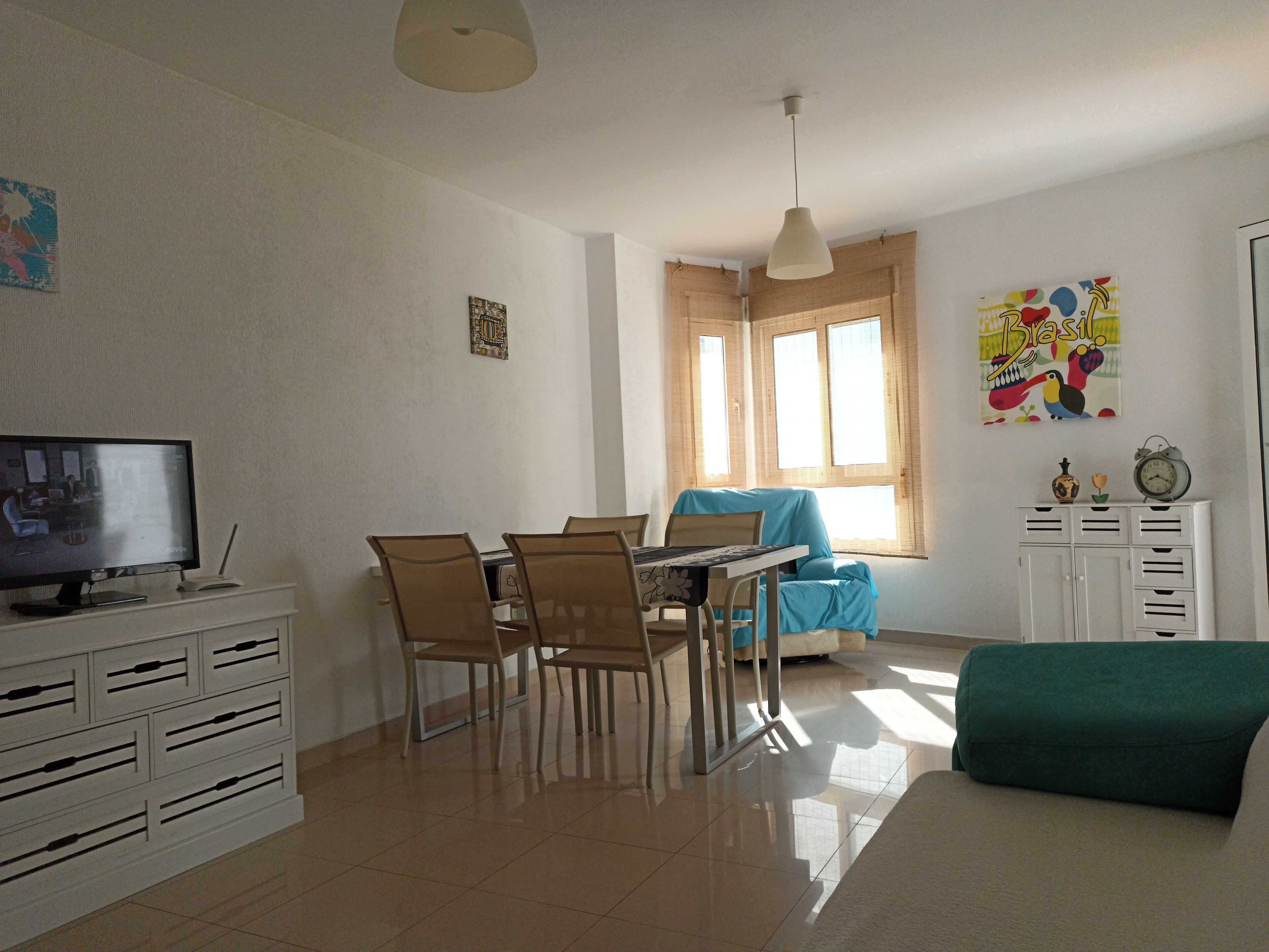 Un comedor con una mesa y sillas, un televisor en un mueble y una ventana con cortinas.