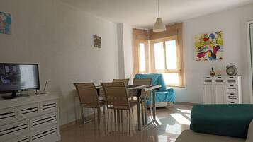 Un comedor con una mesa y sillas, un televisor en un mueble y una ventana con cortinas.