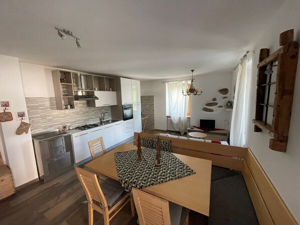 A modern kitchen with white cabinets, a built-in oven, and a dining area with a wooden table and chairs. - Apartment in the mountains, view of the Maddalene chain -Trentino-Alto Adige CIN (Tregiovo)