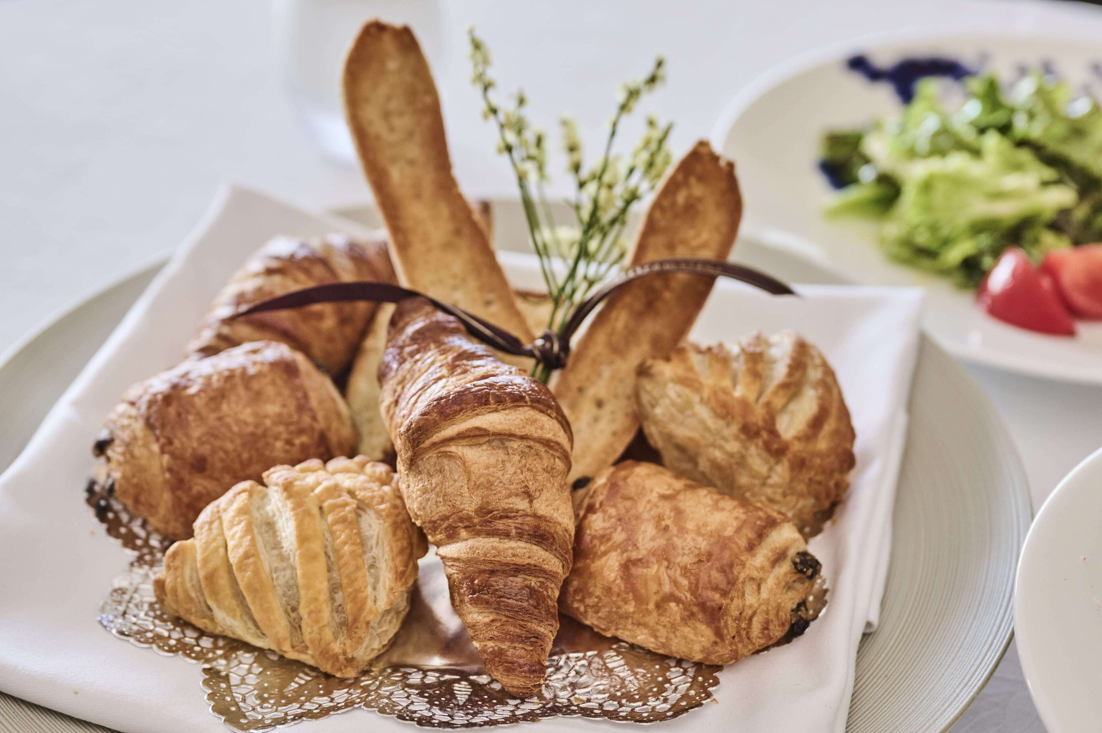 En tallerken med et udvalg af kager, heriblandt croissanter og et chokoladedrys, på en hvid tallerken med blondekant.