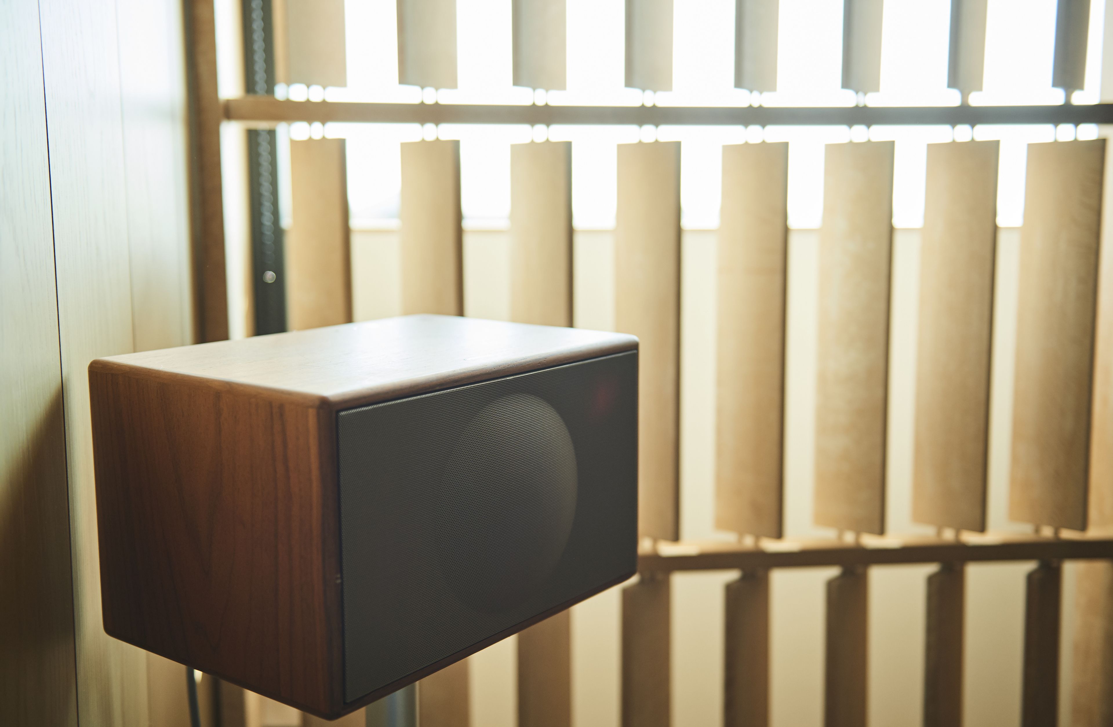 A wooden speaker against a window with vertical blinds.