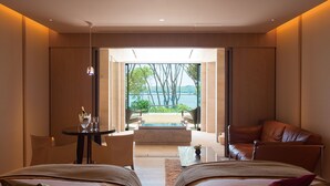 A modern hotel room with two beds, a sitting area with a view of the sea, and a small table with a bottle and glasses. - The Hiramatsu Hotels & Resorts Kashikojima (Shima)