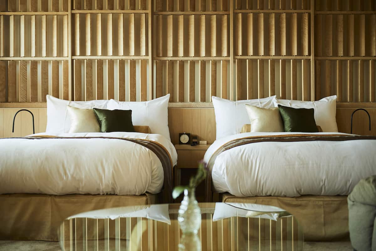 A hotel room with two beds, a wooden headboard, a bedside table, and a vase with flowers.