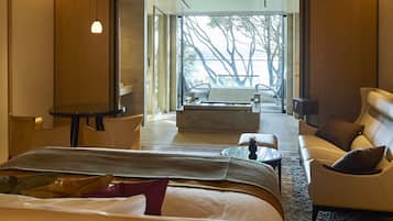 A modern hotel room with a large bed, a sofa, a dining table, and a view of the outdoors.