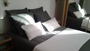 Un lit bien fait, avec une couette blanche et de couleur foncée, deux oreillers et un plaid blanc.
