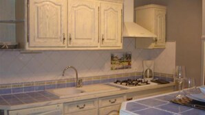 Une cuisine avec des meubles blancs, un évier, une cuisinière et un dosseret carrelé.