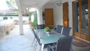 Une terrasse couverte avec une table et des chaises en verre, une porte en bois et un mur en pierre.