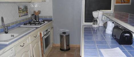 A kitchen with white cabinets, a gas stove, a sink, and a trash bin.