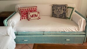 Ein weißes Sofa mit Korpus in Türkisgrün, zwei Kissen mit roten und weißen Mustern und eine Decke in Schwarzweiß.