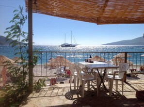 A terrace with a table and chairs, overlooking a beach with umbrellas and a sailboat in the distance. - Beautiful 2 Levels Romantic Luxury Stunning Views, Private Roof  Pool, Spacious  (Kalkan)