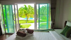 Une chambre d’hôtel avec un lit, une vue sur une piscine et des palmiers, accessible par une porte-fenêtre coulissante, et un ensemble de serviettes posées sur le lit.
