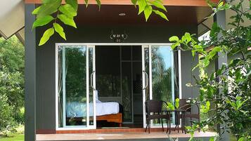 A modern building with a glass door entrance, a bed visible inside, and a small outdoor seating area with chairs and a table.