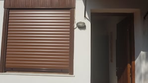 Fachada de edificio con una ventana cubierta por una persiana marrón cerrada y una puerta que da a un interior.