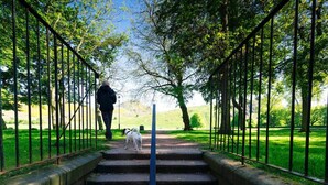 Un sendero bordeado por barandas metálicas que lleva a una zona verde con escalones.