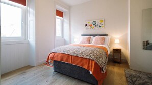 Un dormitorio con cama, mesita de noche, ventana y una obra de arte en la pared.