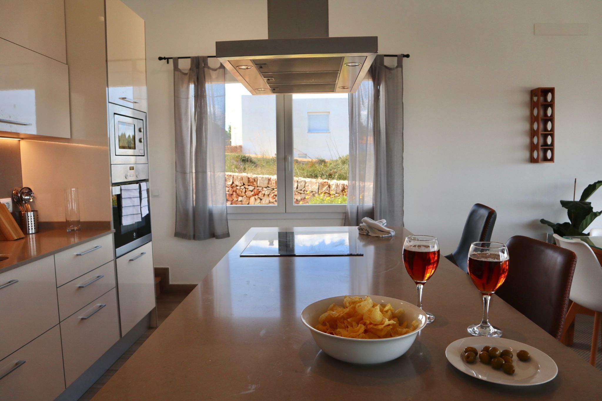 Una cocina moderna con comedor, un amplio ventanal con cortinas y una mesa servida con aperitivos y bebidas.