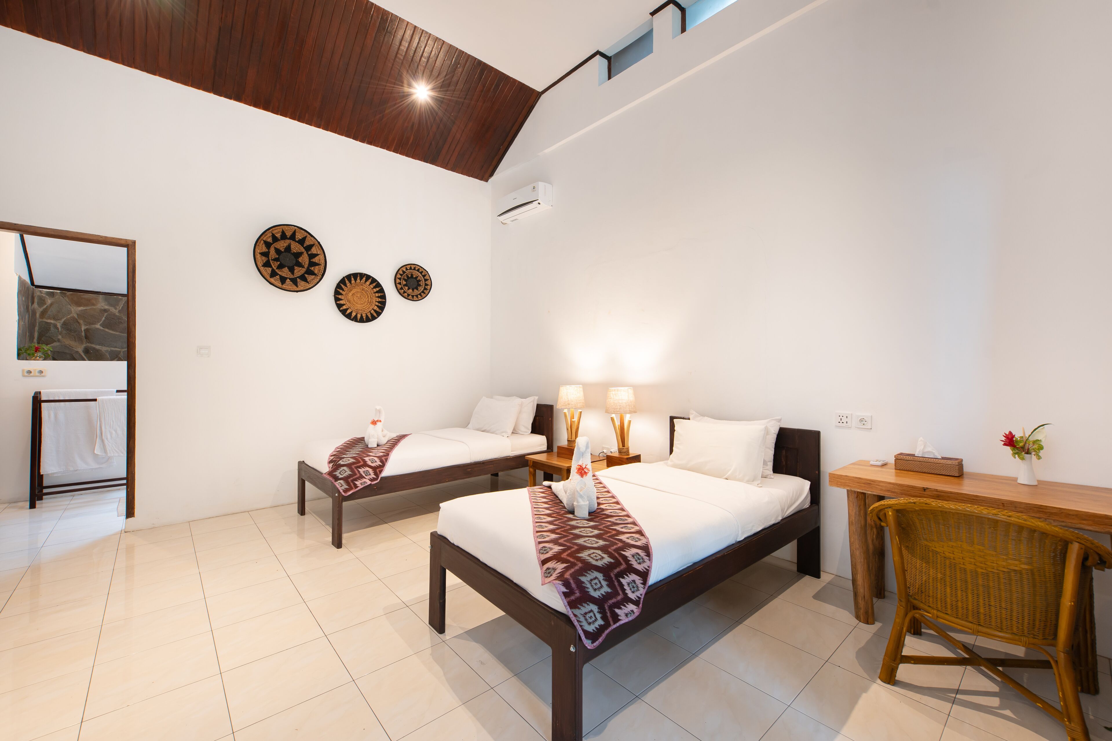 A hotel room with two beds, a wooden desk, and a wicker chair.