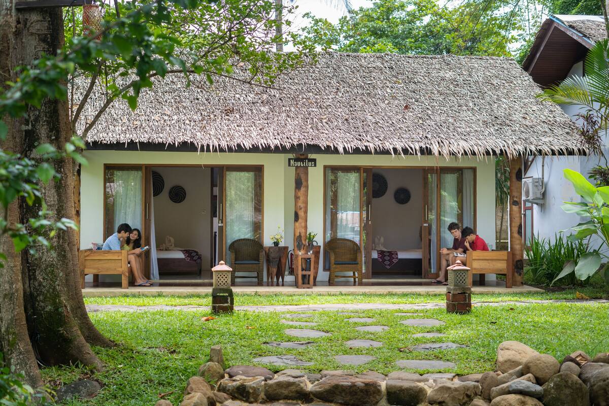 A thatched-roof building with a covered porch, stone pathway, and a small garden area.