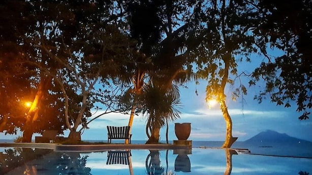 Una piscina infinita con diseño de cuadros, rodeada de árboles y un banco.