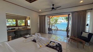 Habitación de hotel con cama, escritorio, sillón, sofá y balcón con vista al mar.