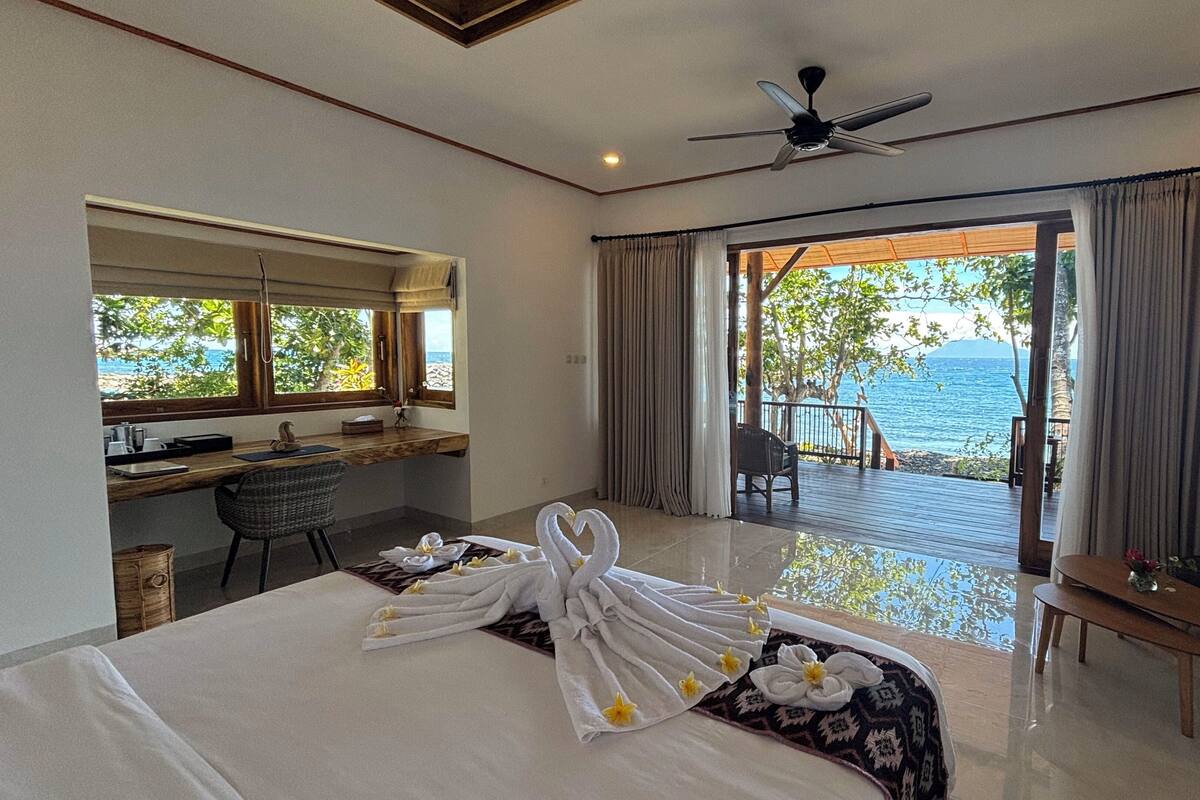 A hotel room with a bed, a desk, a chair, a sofa, and a balcony with a view of the sea.