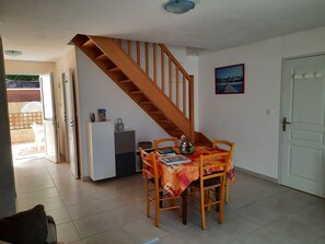 Ein Essbereich mit Holztisch und -stühlen, eine kleine Küchenzeile inklusive Kühlschrank und Spüle sowie eine Treppe zu einer oberen Ebene.
