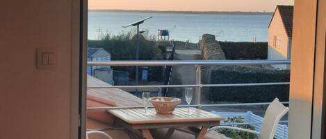 A balcony with a table and chairs, overlooking a body of water and a distant shoreline.