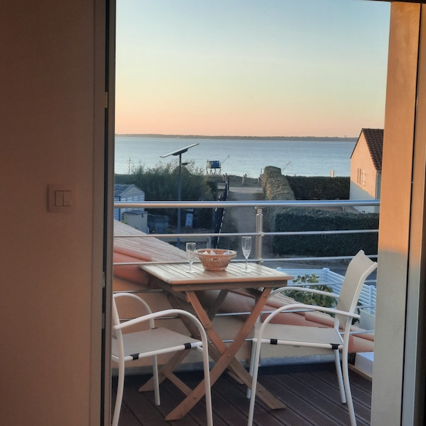 A balcony with a table and chairs, overlooking a body of water and a distant shoreline.