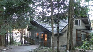A cabin with a deck, surrounded by trees and a gravel path. - Neil Bay Waterfront Family And Pet Friendly Property!<br>PCUP00-13-0010  (Roche Harbor)
