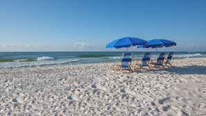 Una playa con cuatro sillas azules y dos sombrillas azules.
