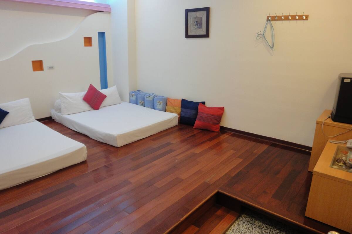 A room with two single beds, a wooden floor, a small table with a speaker, and a wall-mounted coat rack.