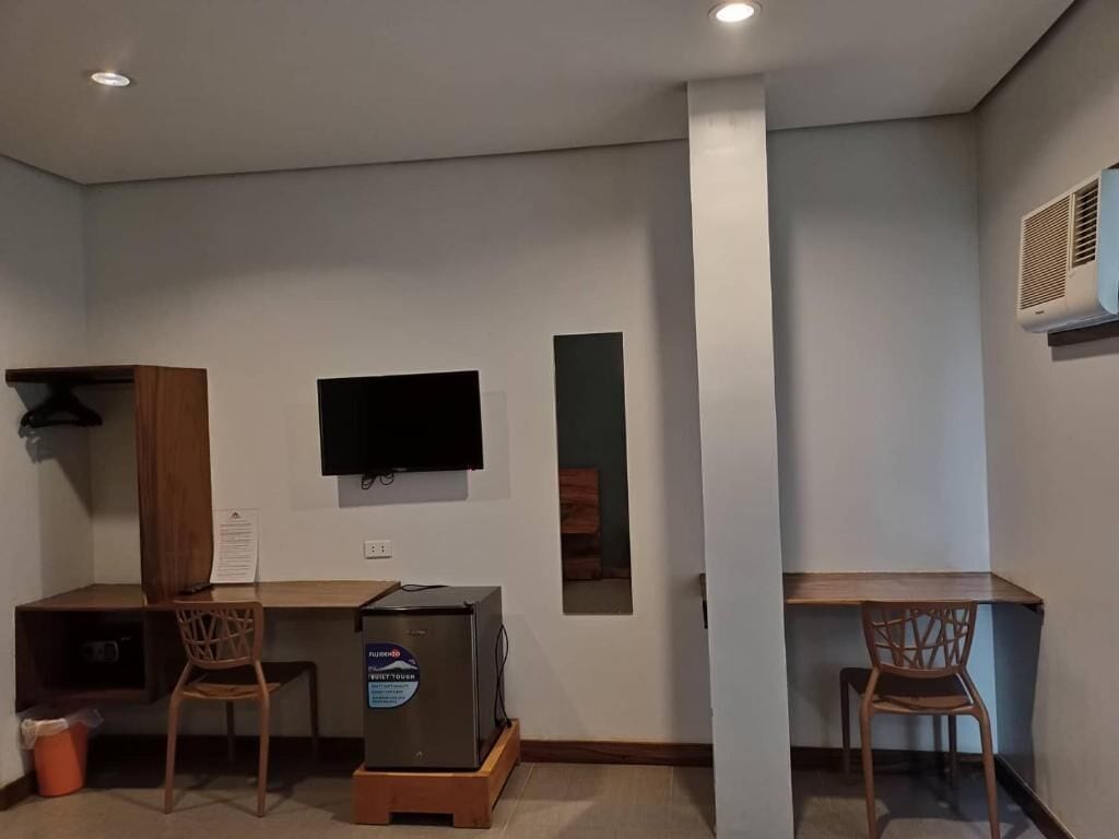 A room with a desk, two chairs, a television, and an air conditioning unit.