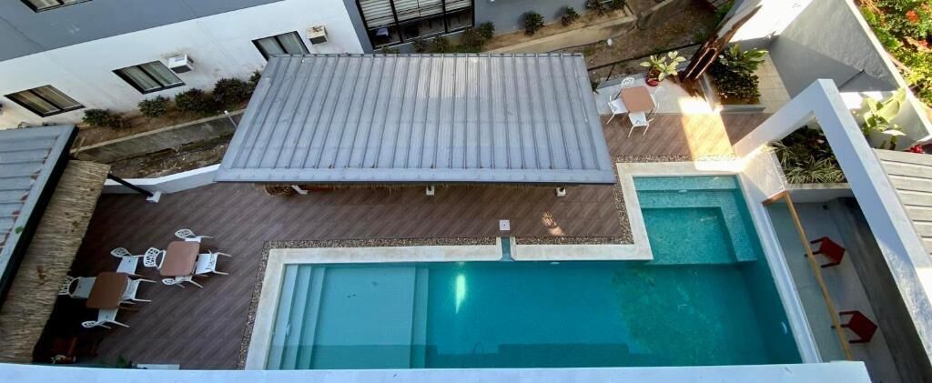An outdoor swimming pool with a deck area, surrounded by a white fence, and a covered patio area with seating.