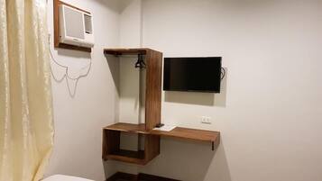 Una camera da letto con un letto, una scaffalatura in legno, una TV a parete e un condizionatore d'aria.