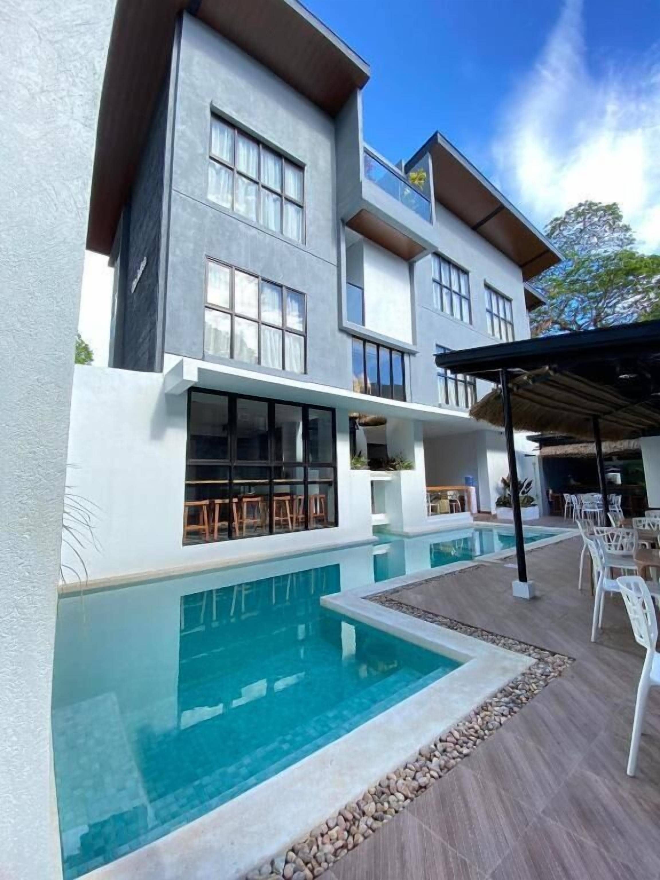 Um edifício moderno de dois andares com piscina, área de estar externa e um pátio coberto.