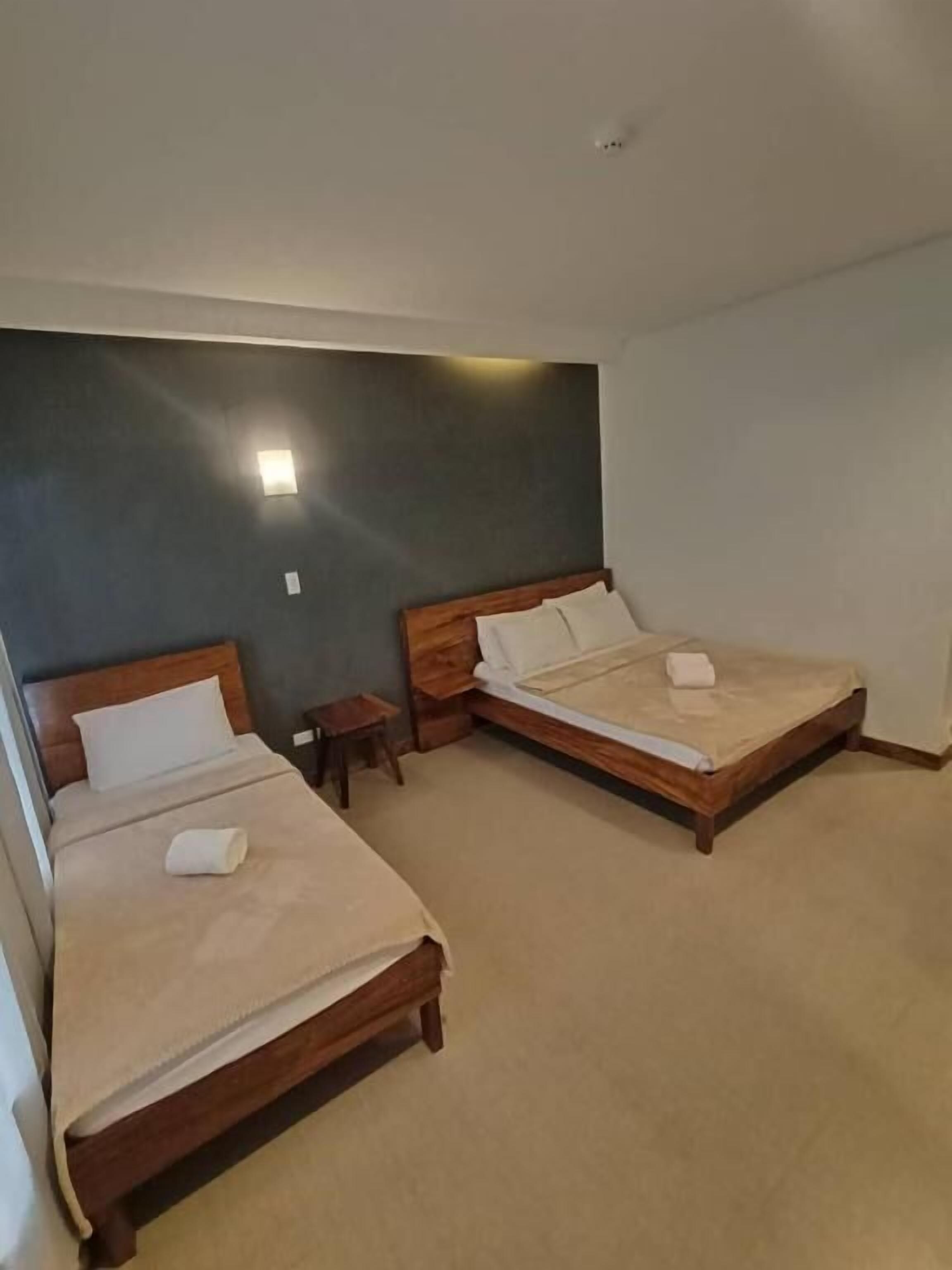 A room with two wooden beds, each with a white pillow and a blanket, and a small bedside table.