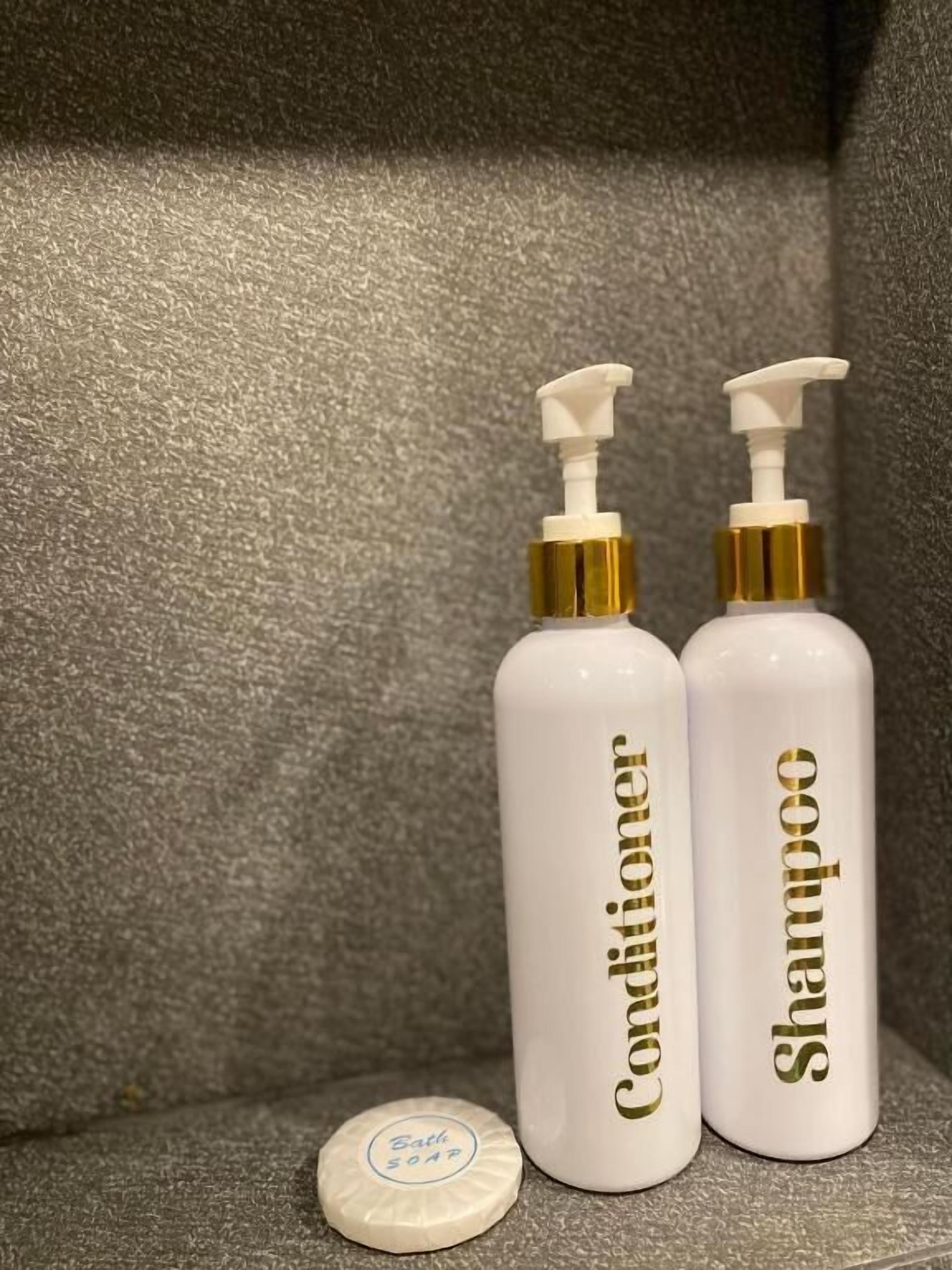 Two bottles of conditioner and shampoo with pump dispensers, and a bottle cap on a textured surface.