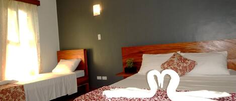 A hotel room with two beds, a dark wall, a bedside table with a plant, and a window with curtains.