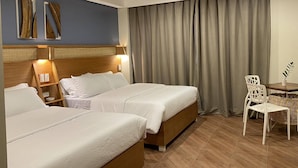 Hotellihuone, jossa on kaksi sänkyä, puinen pääty, työpöytä tuolilla sekä ikkuna, jossa on verhot.