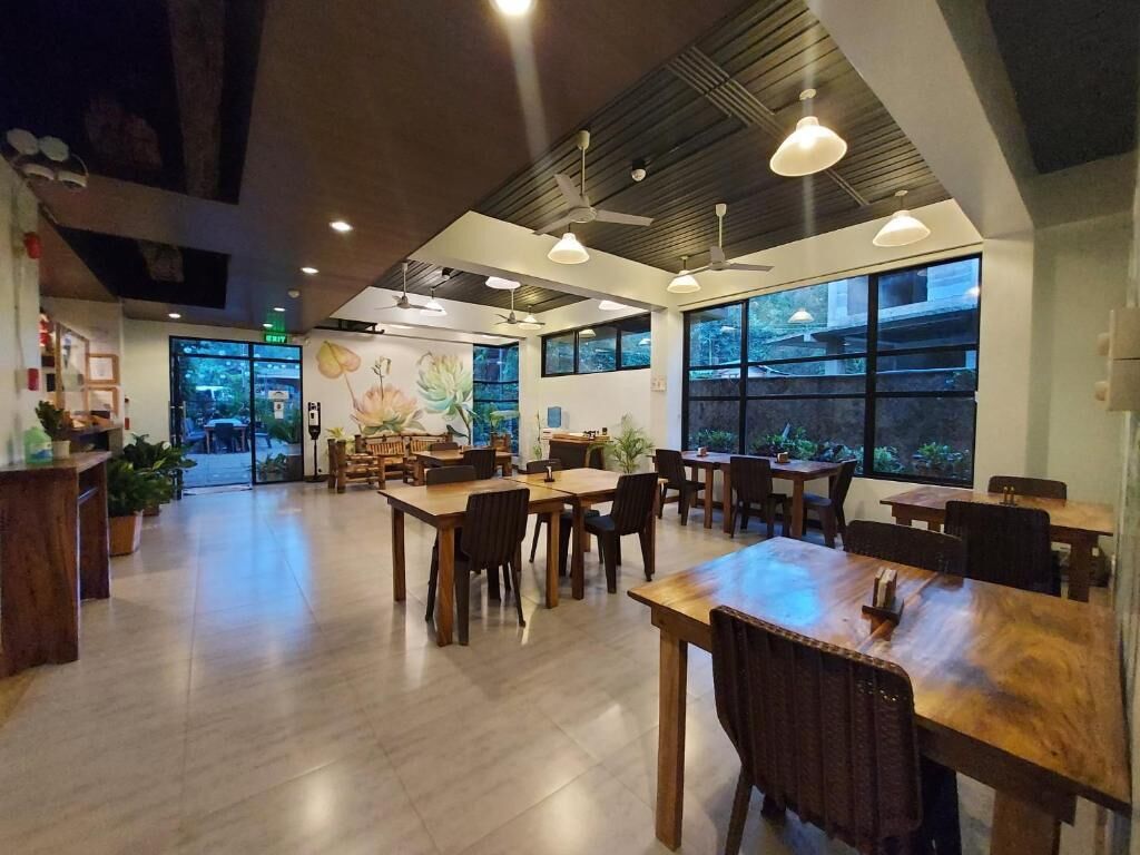 A spacious indoor area with multiple wooden tables and chairs, large windows, and ceiling fans.