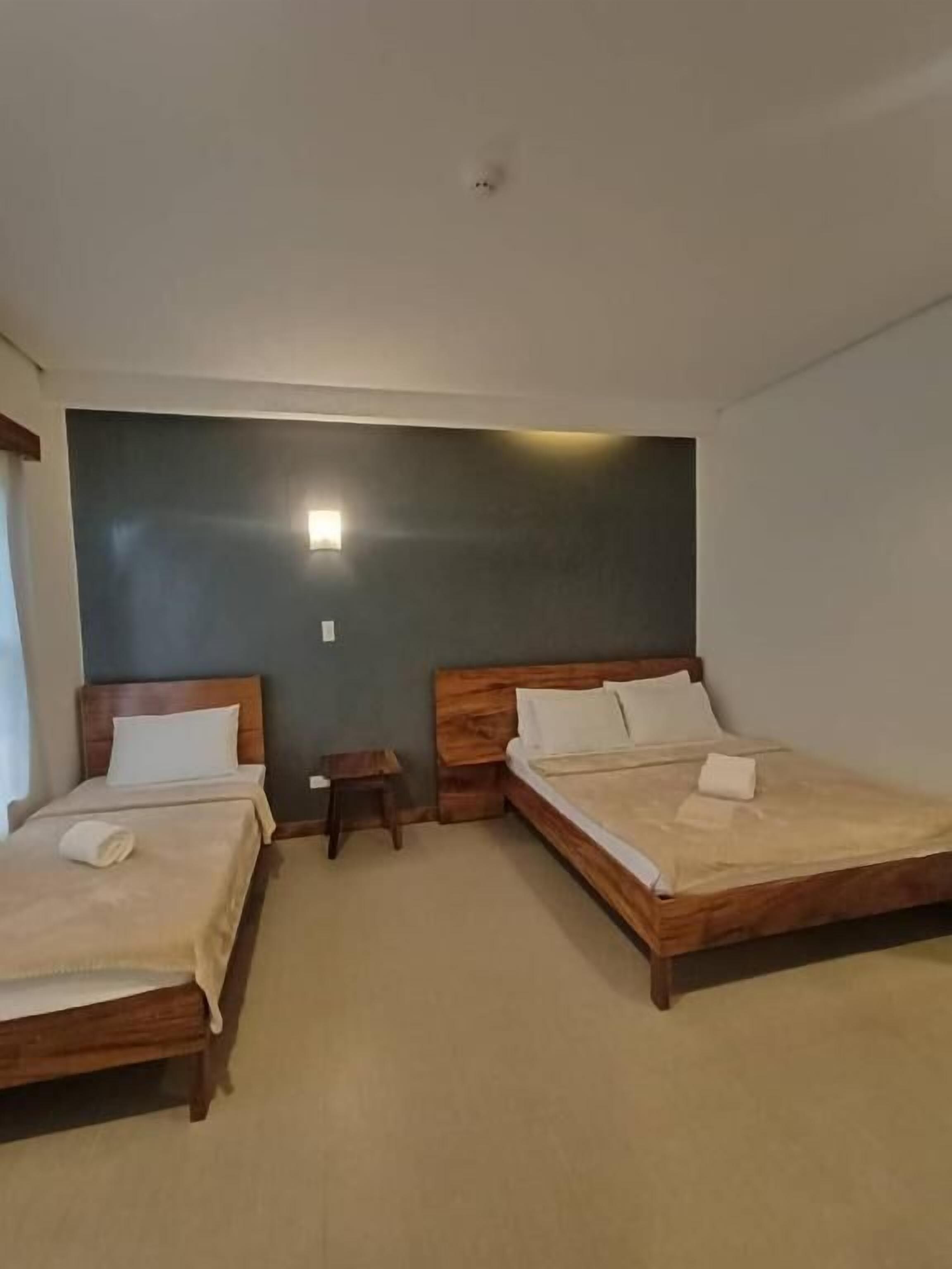 A room with two wooden beds, a small bedside table, and a wall-mounted light fixture.