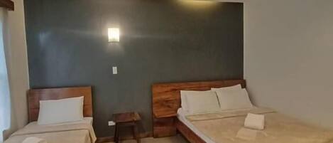 A room with two wooden beds, a small bedside table, and a wall-mounted light fixture.