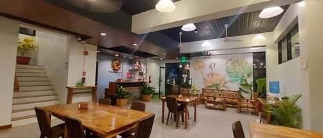 A restaurant with wooden tables and chairs, a staircase, and a mural on the wall.
