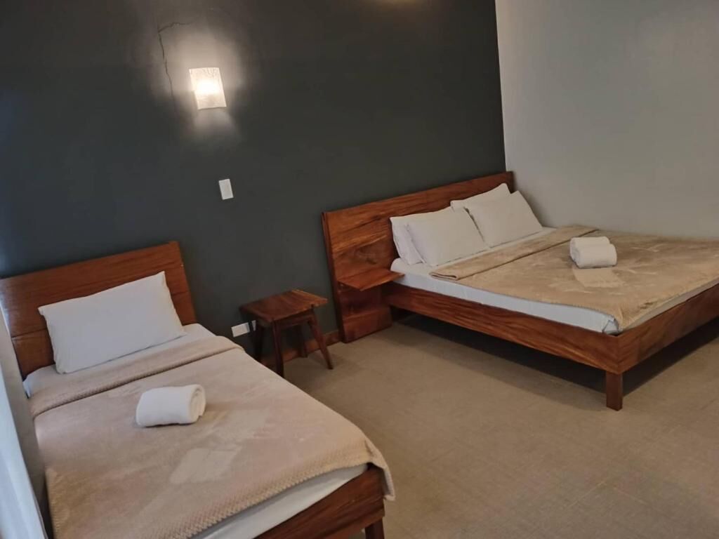 Zwei hölzerne Betten mit weißen Leinen, ein kleiner Nachttisch und eine an der Wand befestigte Lampe.