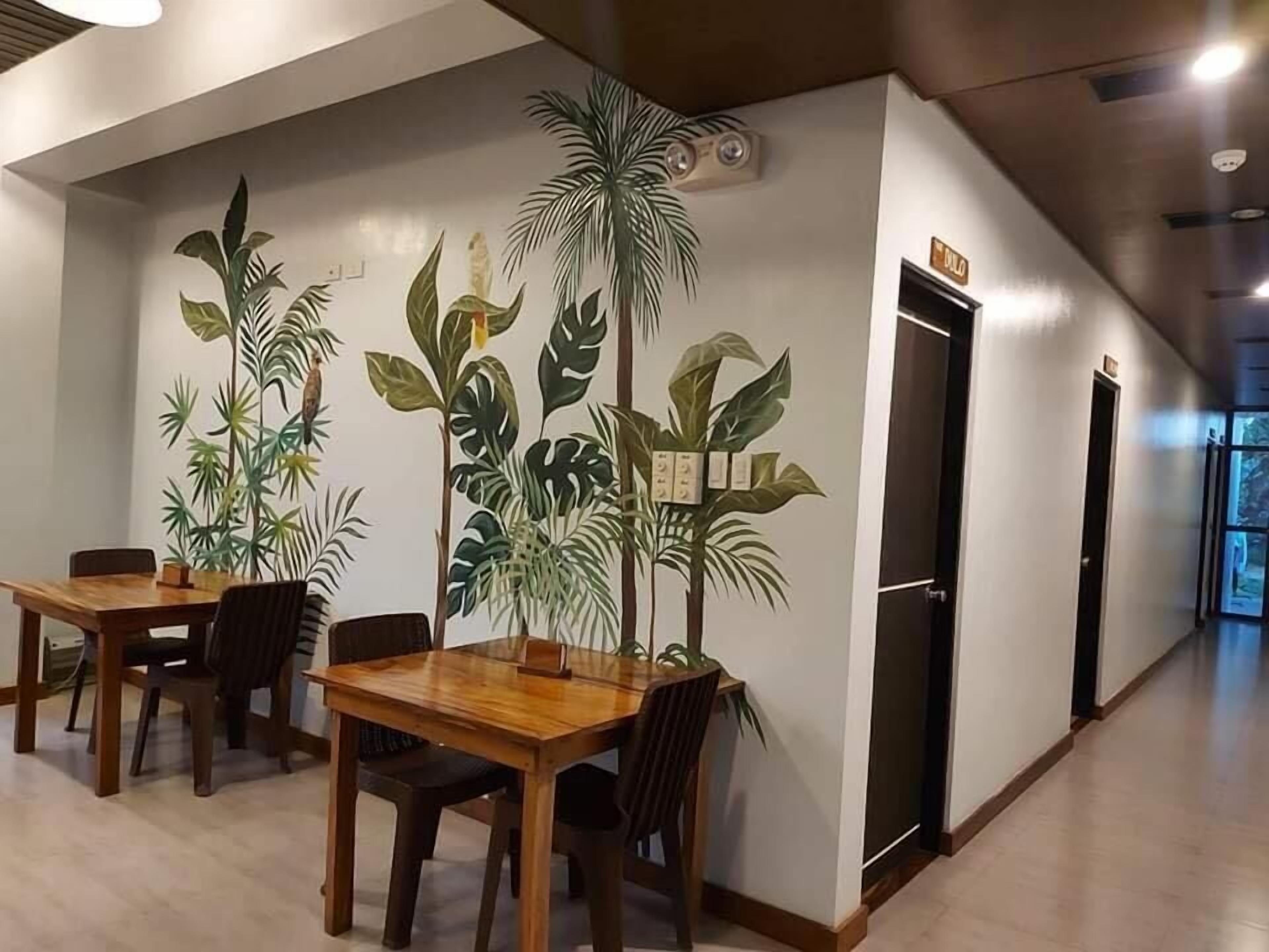 En gang med et træbord og stole, en plante på væggen og en dør med et skilt.
