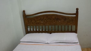 Een net opgemaakt bed met een houten hoofdbord, een opgevouwen witte handdoek op het bed en een wandgemonteerde airconditioning met een stopcontact.