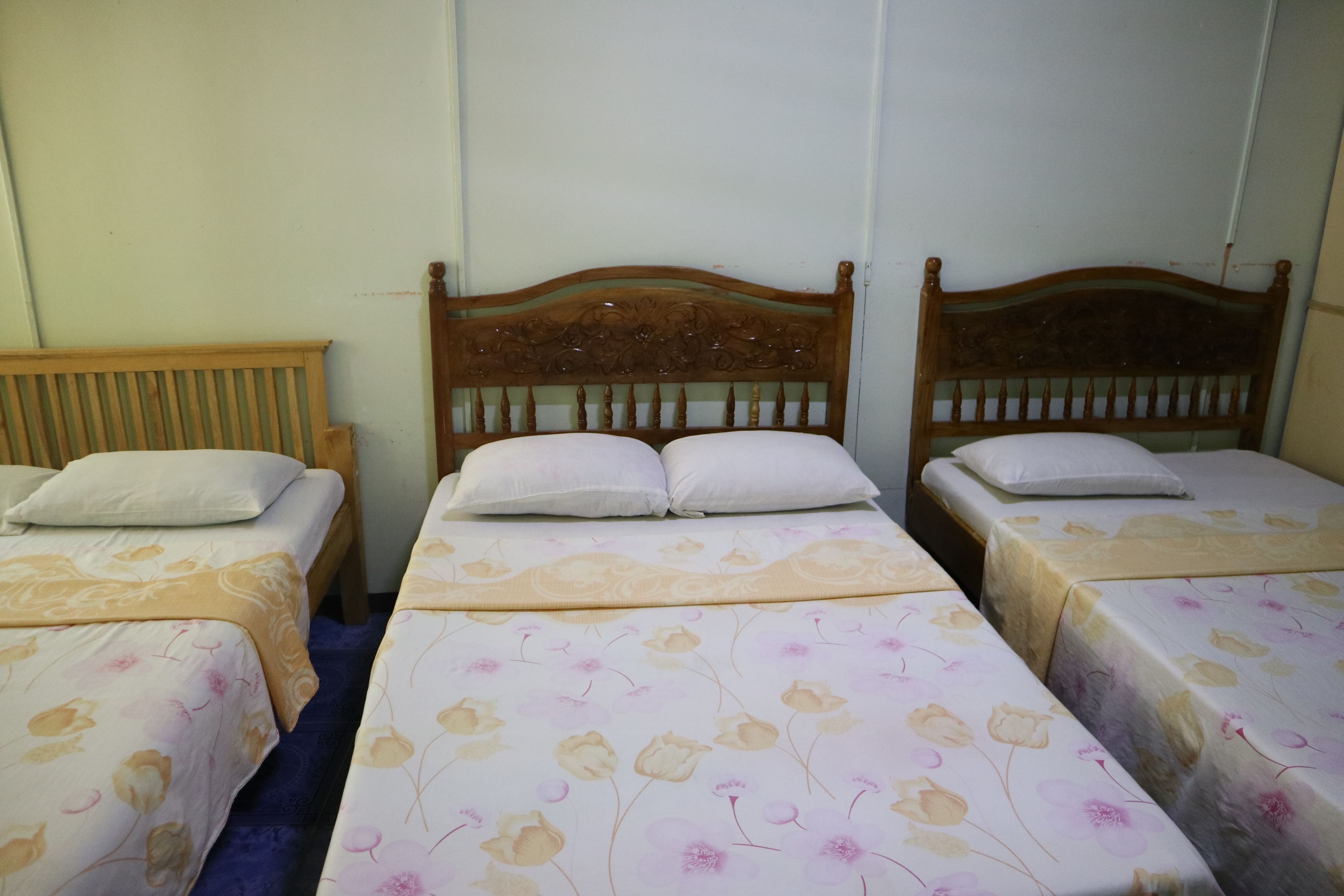 Quarto com três camas de solteiro, cada uma com cabeceira de madeira e roupa de cama estampada com flores.