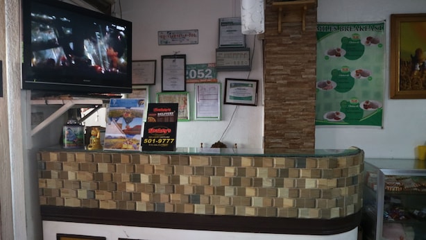 Een restaurantinterieur met een balie, een televisie, ingelijste certificaten en een menuposter.